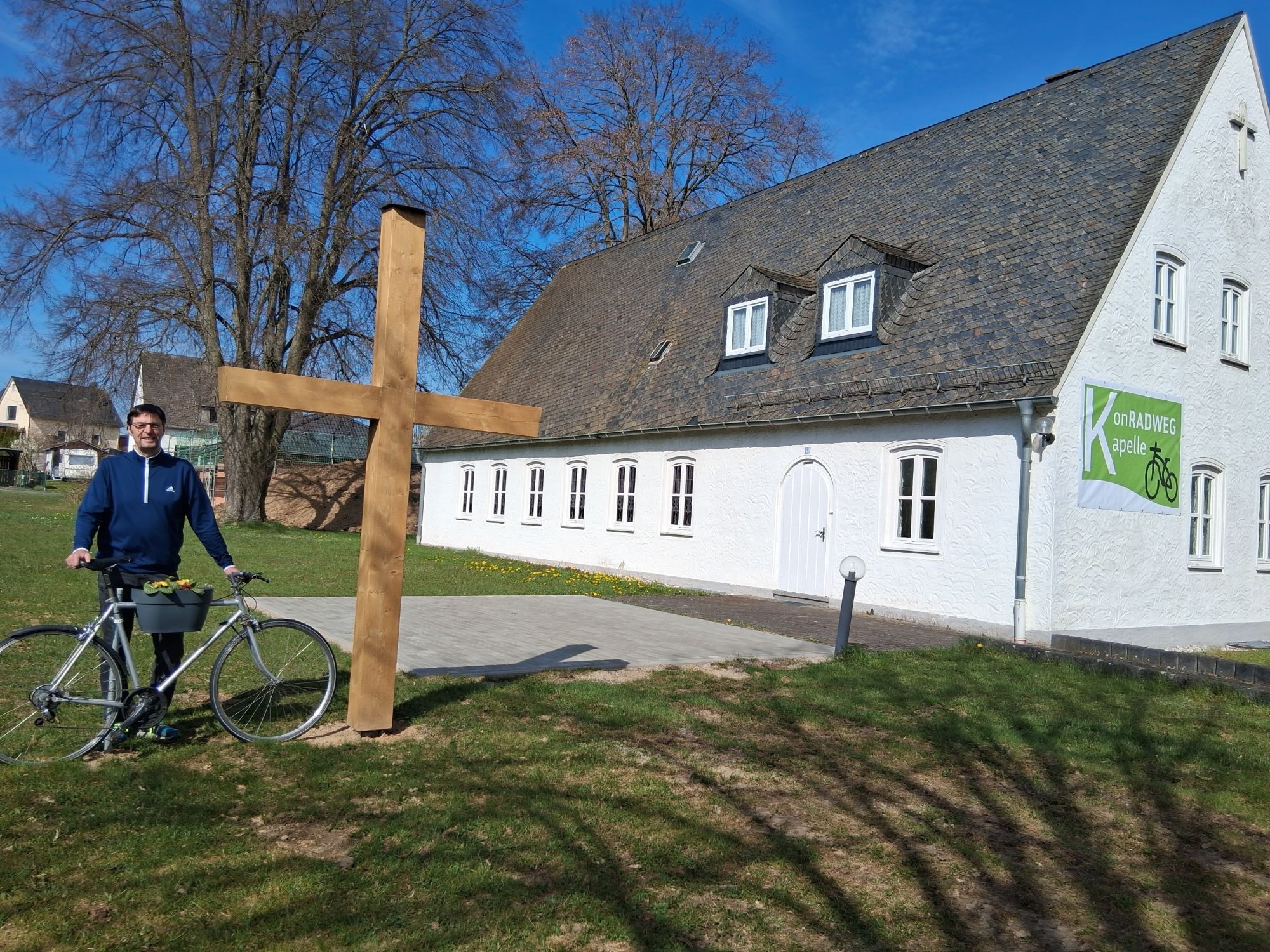 Diakon Franz Jahn mit Fahrrad bei dem neuen Holzkreuz vor der KonRADWEG-Kirche
