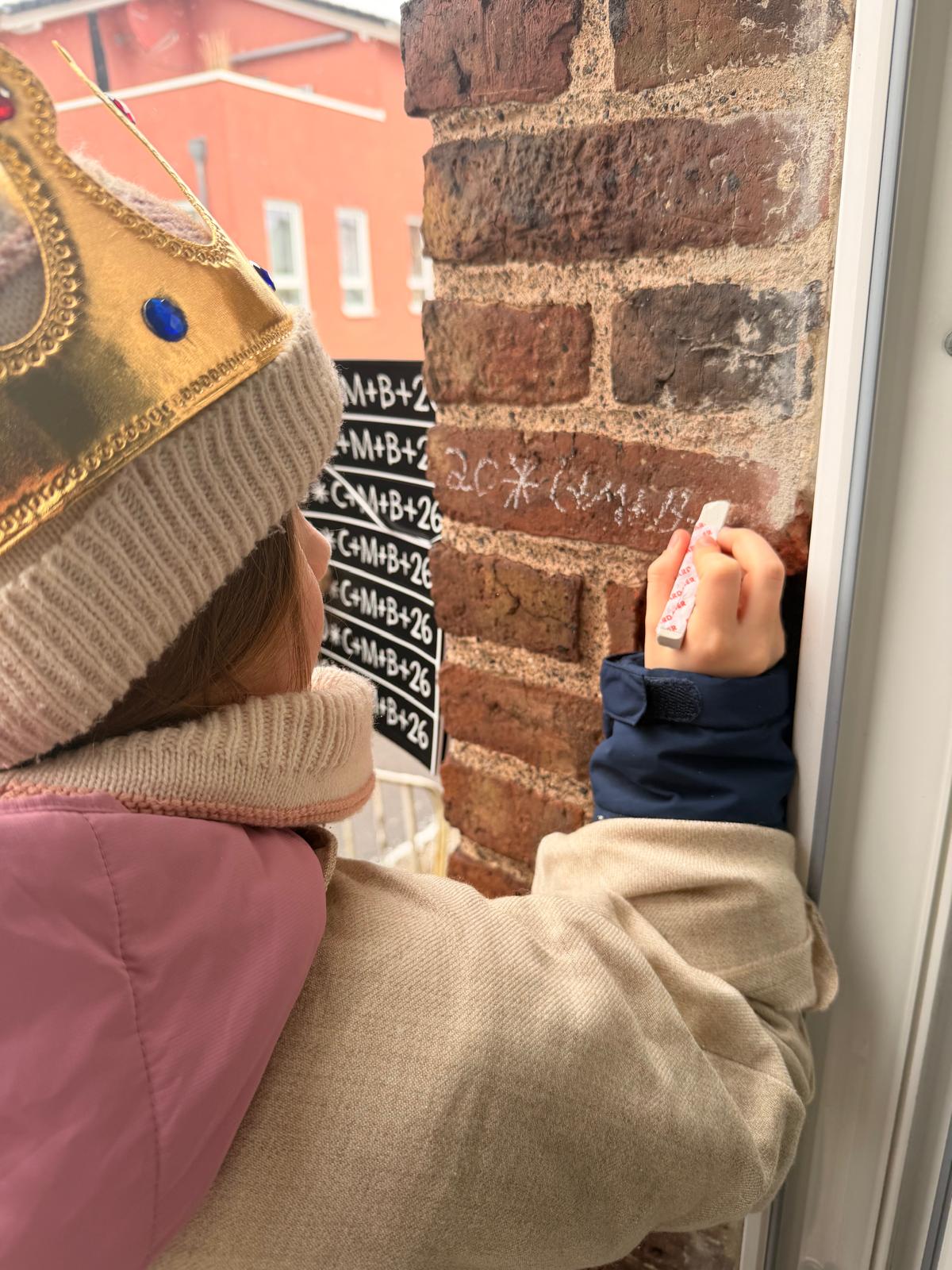 So geht es! Eine Sternsingerin schreibt den Segensspruch an die Tür!